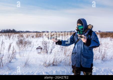 Caucasian Male in the blue jacket launching a flying drone with a remote controller in his hand on winter field. Stock Photo