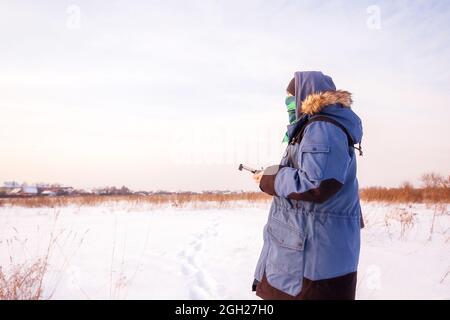 Caucasian Male in the blue jacket launching a flying drone with a remote controller in his hand on winter field. Stock Photo