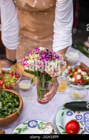 Woman arranging dining table with bouquet of flowers. Setting table for garden party Stock Photo