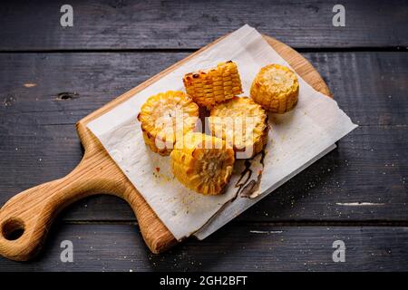 Top view grilled corn on the cob with oil and salt on a wooden board, close-up on a dark wooden background. Delicious grilled corn. Copy space Stock Photo