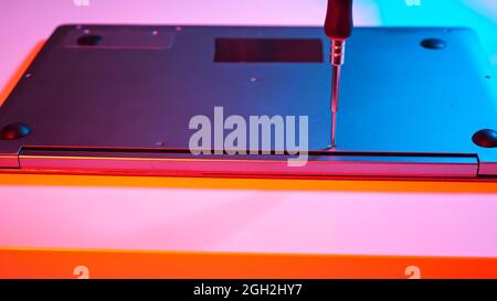 Unrecognizable master screwing bolts into laptop lid in muted red and blue light Stock Photo
