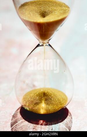 Gold Sand running through the bulbs of an hourglass measuring the passing time in a countdown to a deadline, on a light pastel reddish background - sh Stock Photo