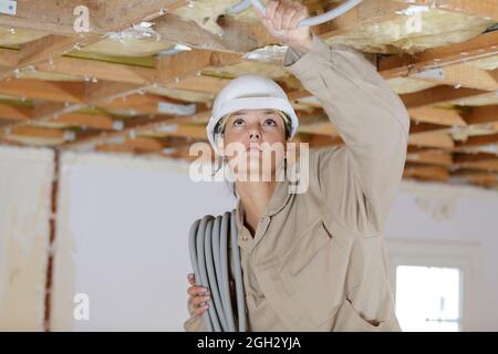 woman holding cables overhead in roofspace Stock Photo