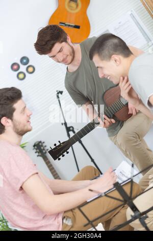 three young people in studio composing music one holding guitar Stock Photo