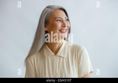 Joyful lmiddle aged lady wearing beige blouse stands on light background Stock Photo