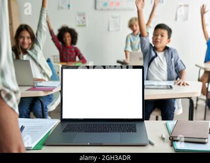 Laptop computer white blank empty mockup screen on teachers table in classroom. Stock Photo