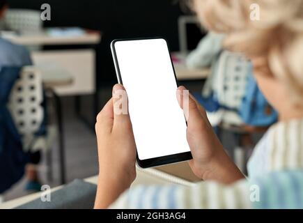 Kid boy junior school student using phone with mockup screen in classroom. Stock Photo