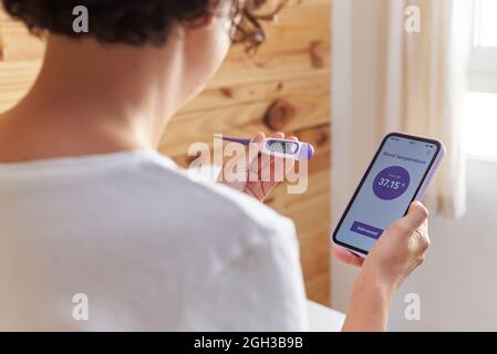 An unrecognizable woman writes down her basal temperature on her smartphone app Stock Photo