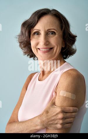 Smiling older senior happy woman showing bandage after getting vaccination. Stock Photo