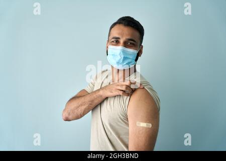 Happy Indian man wearing face mask showing bandage after getting vaccination.