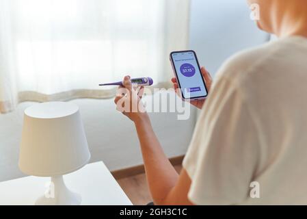 An unrecognizable woman writes down her basal temperature on her smartphone app Stock Photo