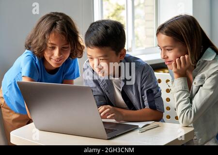 Diverse happy school kids using laptop computer together in classroom. Stock Photo
