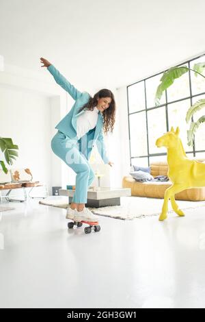 Vertical photo.Vertical photo of business woman riding skateboard dressed in office worker outfit at home. Office worker taking a break, skating Stock Photo