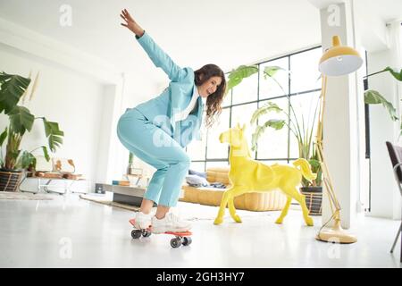 Business woman riding skateboard dressed in office worker outfit at home. Office worker taking a break, skating wildly around the office. Funny of Stock Photo