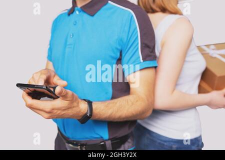 Cropped photo of a postman and a woman blonde standing back to back, postman touching the mobile phone in his hand and woman holding the package. Stock Photo