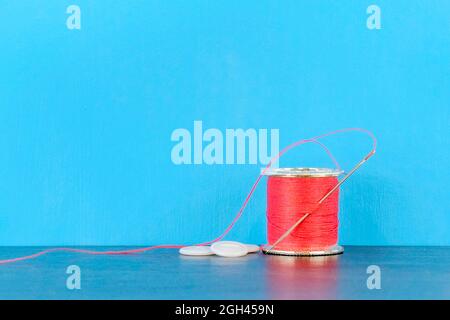 Spool of red cotton with needle and three buttons on light blue background Stock Photo