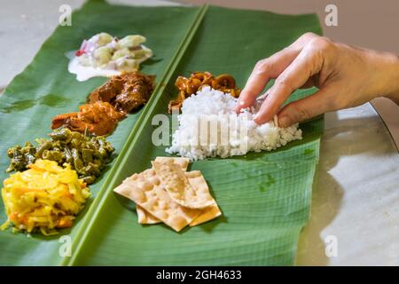 Person enjoying Indian banana leaf rice consisting mutton curry, squid, prawn, papadam and various vegetables Stock Photo