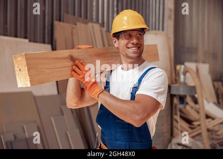 Cheerful worker carrying timber wood plank at construction site Stock Photo