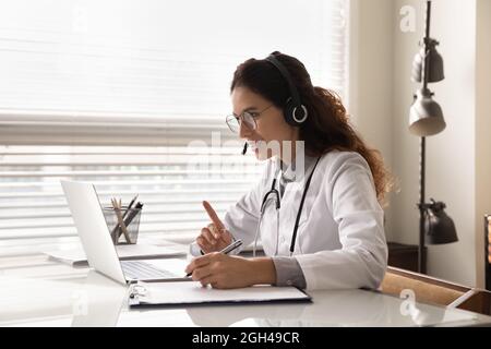 Happy attentive general practitioner in headset using laptop Stock Photo