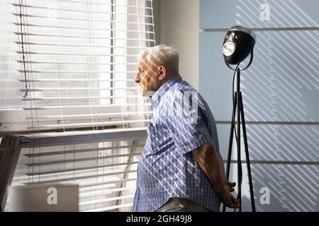Thoughtful sad senior 80s man looking out of window Stock Photo