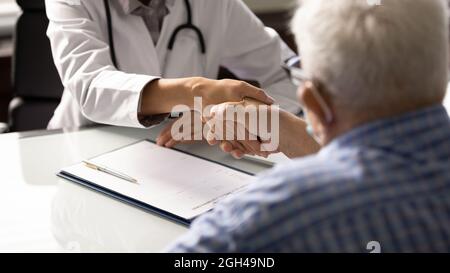 Senior man visiting doctor, shaking hands with young female therapist Stock Photo