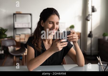 Happy businesswoman using smartphone at office desk, reading message Stock Photo