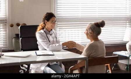 Older senior female patient and young doctor shaking hands Stock Photo