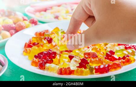 Hand takes colorful gummy bears candies of the plate. Close-up. Jelly treats for children and adults.
