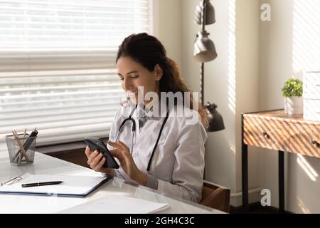 Happy young general practitioner chatting online on mobile phone Stock Photo