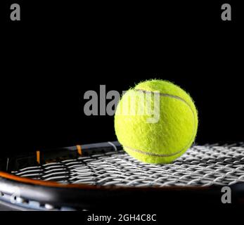 close up of tennis ball on string or net of tennis racquet, racket, on black background for sport for exercise hobby and lifestyle with tennis equipme Stock Photo
