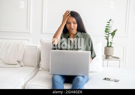 Upset and frustrated young indian woman using laptop for remote work from home, nervous about mistakes, stressful job, mixed-race female student has problem with task holding head with desperation Stock Photo