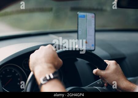 Navigator in car vehicle transportation commuter. Driver man using mobile phone navigator app while driving car. Hands on steering wheel Stock Photo