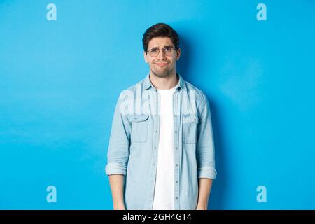 Skeptical and doubtful guy in glasses, looking confused at something strange, blue background Stock Photo