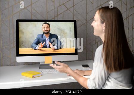 Young woman talking online with an Indian man, support service representative or colleague via video connection on the laptop, female using computer app for virtual communication, rear view Stock Photo