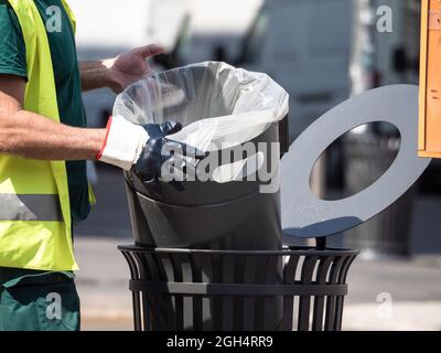 street sweeper with reflective life jacket and rubber gloves replaces the bag in a waste basket Stock Photo