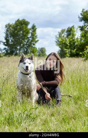 Owner girl playing with her siberian husky at field. Happy smiling woman with dog have a good time on weekend activity outdoors Stock Photo