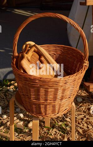 On a wooden stool there is a wicker basket with wooden cutting boards. Stock Photo