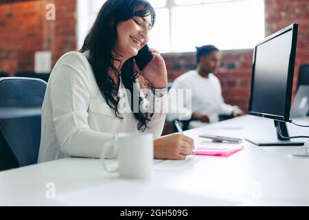 Smiling businesswoman taking a phone call in the office. Creative businesswoman connecting with her business clients while sitting in a modern office. Stock Photo