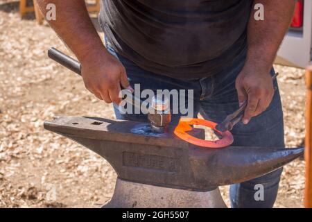 A blacksmith, farrier, creating and shaping a horseshoe on an Anvil, with a hammer, Spain. Stock Photo