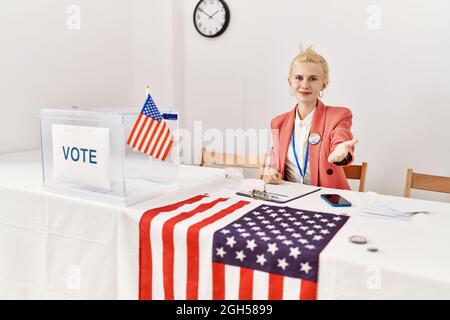 Beautiful caucasian woman working at political campaign smiling cheerful offering palm hand giving assistance and acceptance. Stock Photo