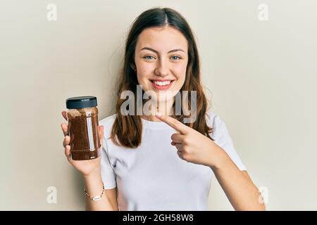 Young brunette woman holding soluble coffee smiling happy pointing with hand and finger Stock Photo