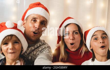 Happy family doing selfie with mobile phone wearing Santa Clause hats during Christmas eve - Focus on mother face Stock Photo
