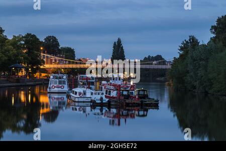 Various boats including river cruisers moored at twilight on the River Dee in Chester, under the Queens Park Bridge in September 2021. Stock Photo