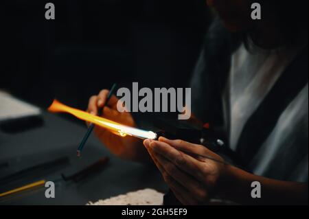 work of a glassblower. Women's hands hold the burner and melt the glass. Low key. Soft selective focus, noise. Stock Photo