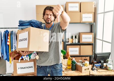 Handsome middle age man holding donations box for charity at volunteer stand looking unhappy and angry showing rejection and negative with thumbs down Stock Photo