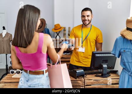 Young latin customer man paying to shopkeeper using credit card at clothing store. Stock Photo