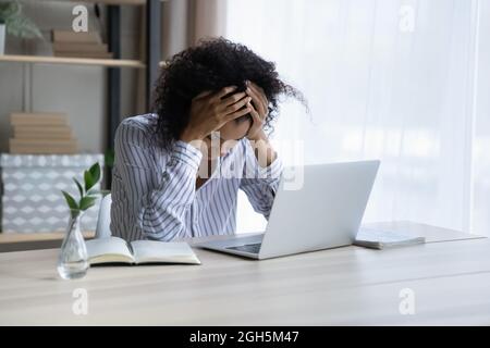 Depressed upset black female sit at workplace hug head Stock Photo