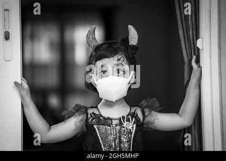 A grayscale shot of a Southeast Asian girl wearing her costume and also a facemask on Halloween Stock Photo