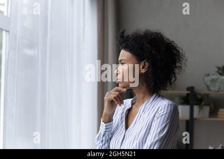 Contemplative young black businesswoman look at window touch chin thinking Stock Photo