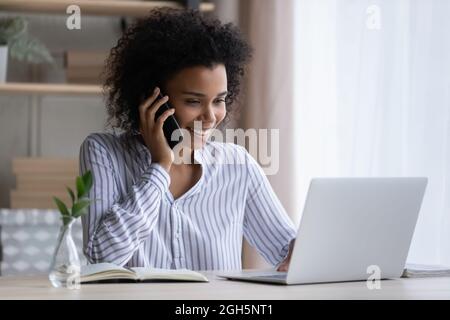 Black female office employee multitasking talking by phone using laptop Stock Photo